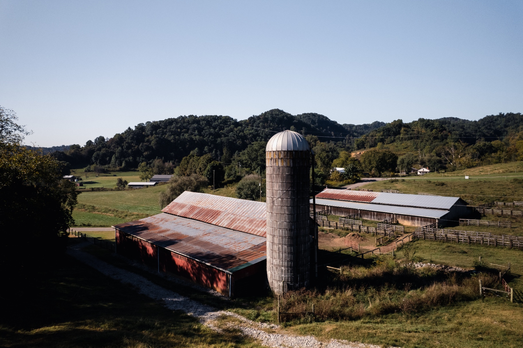 A working farm with a red barn, tall silo, and rolling green hills in Hawkins County, Tennessee under a clear blue sky.