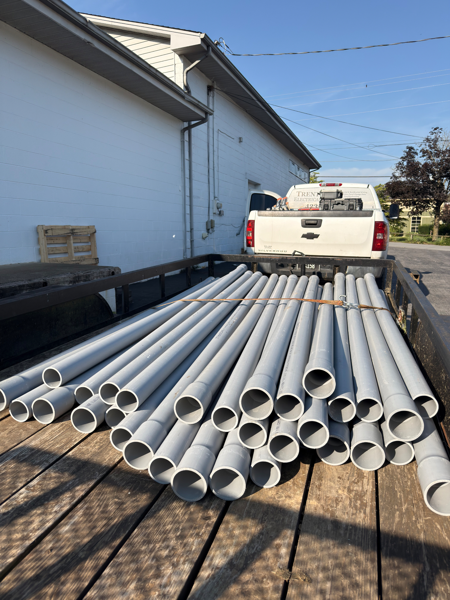 Stack of gray PVC electrical conduit loaded on a Trent Electrical Silverado flatbed for an underground service job