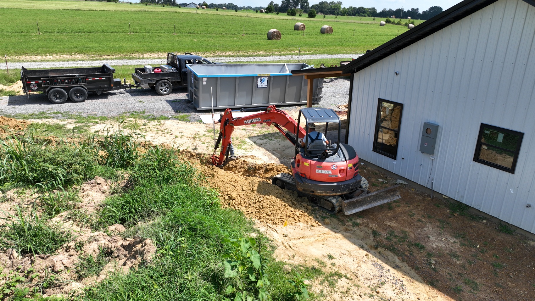 Kubota mini excavator digging an electrical trench next to a metal shop building
