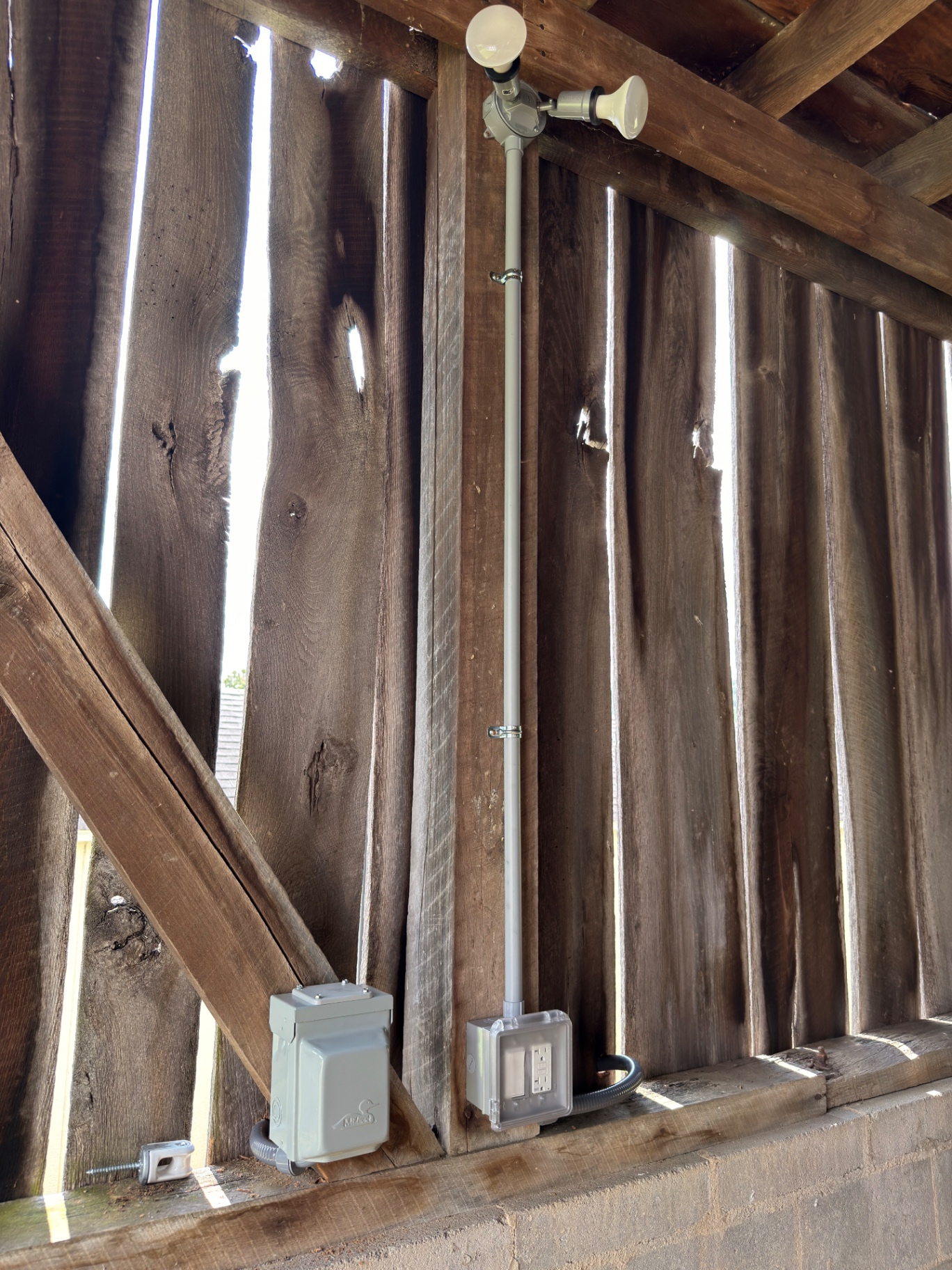 Interior barn wiring with rigid conduit, weatherproof GFCI receptacle, disconnect, and overhead LED barn light on rough-sawn framing
