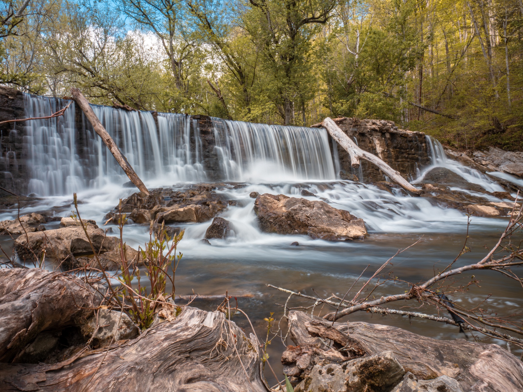 A wide waterfall cascading over rocky ledges surrounded by green spring trees in Hawkins County, Tennessee.