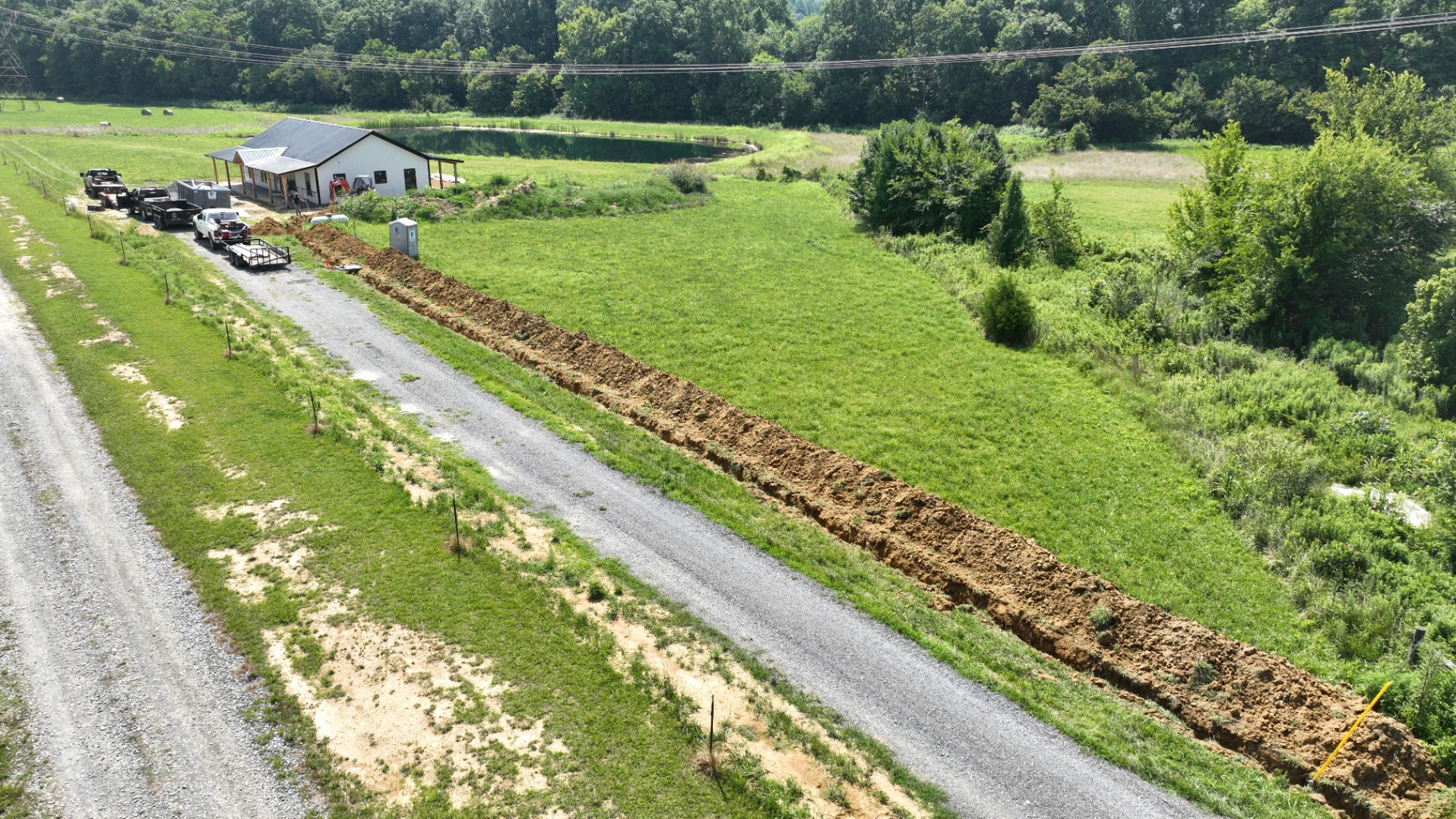 Aerial view of a long electrical trench running from a metal shop across a rural field