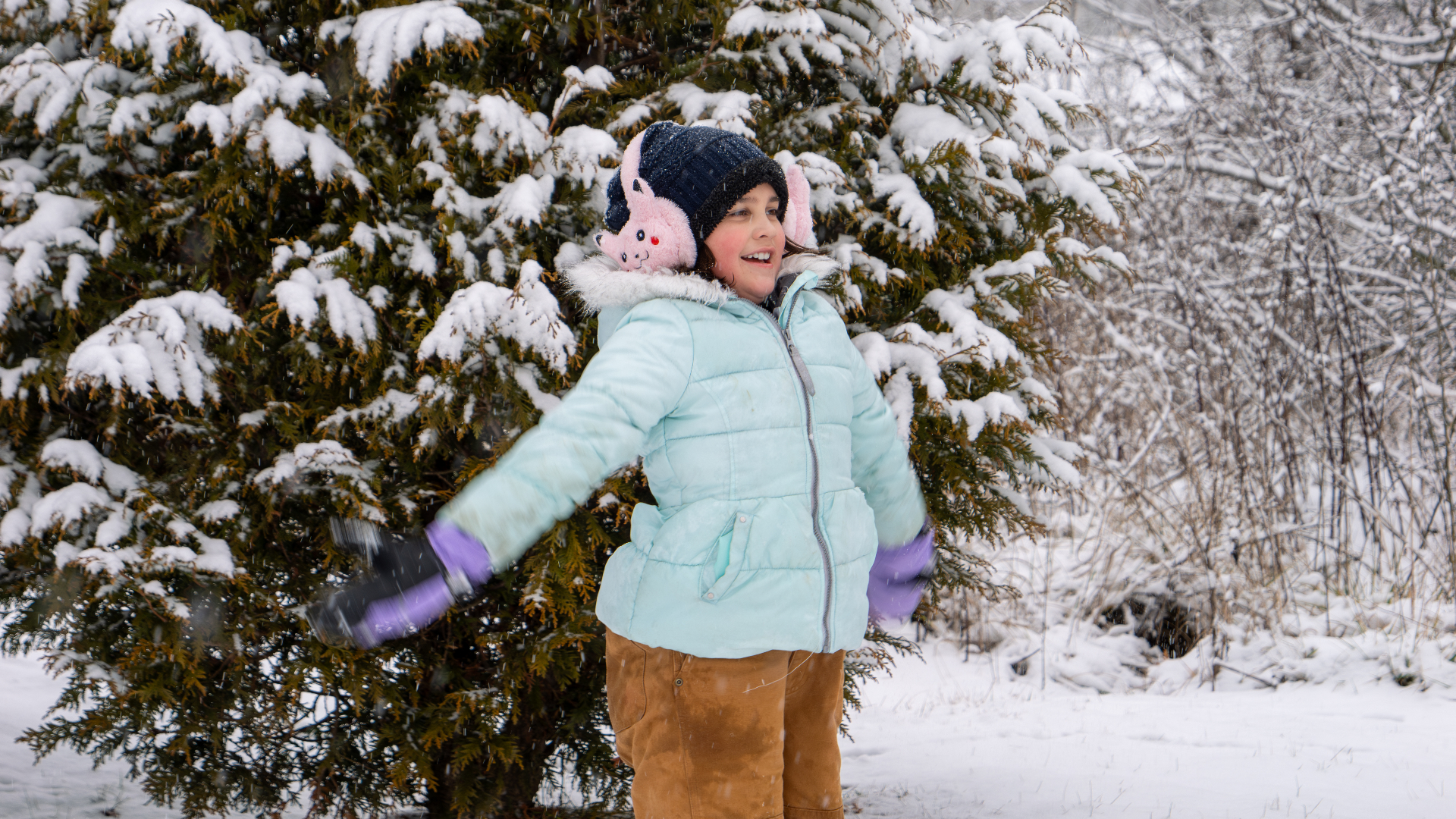 A child in a light blue winter coat and knit hat playing in fresh snow in front of snow-covered evergreen trees in Hawkins County, Tennessee.