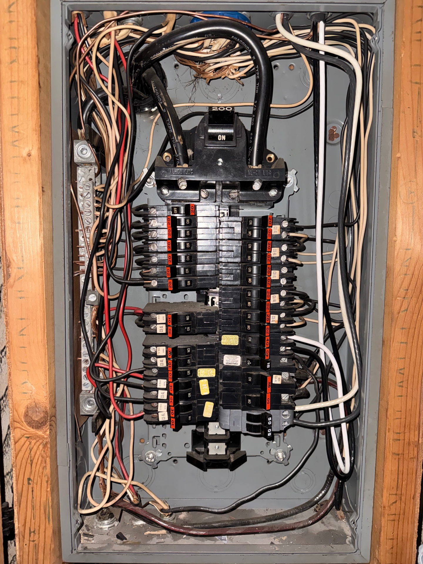 Inside view of an older 200 amp panel with the dead front removed, showing tangled branch-circuit conductors and aging breakers.